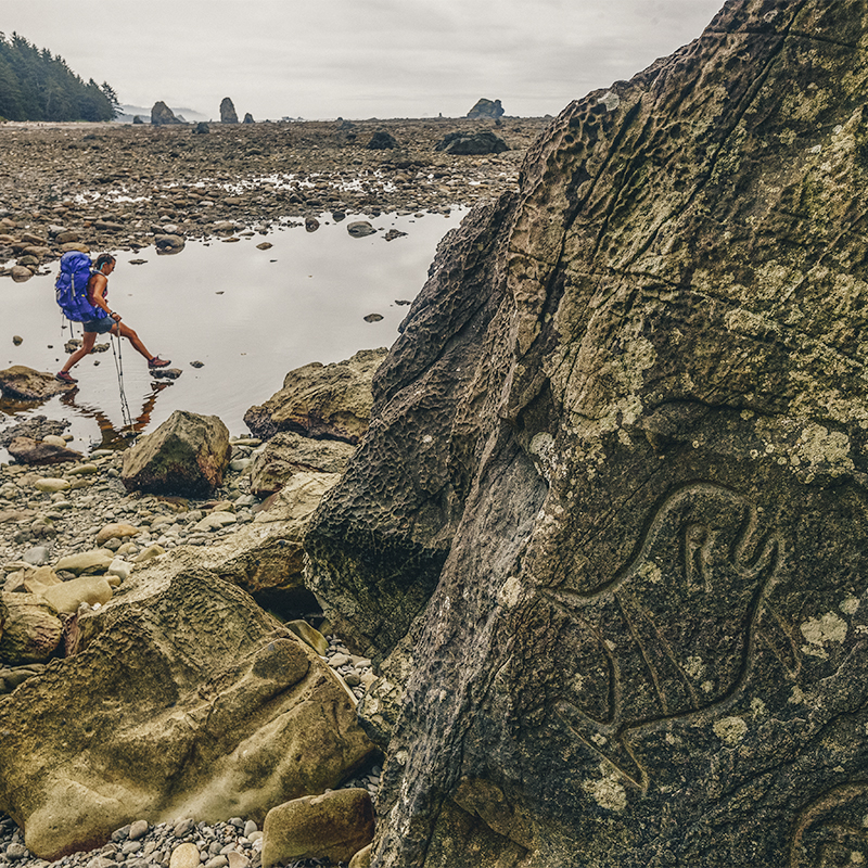  A woman hikes past a sacred site of petroglyphs along the coast in Olympic National Park.