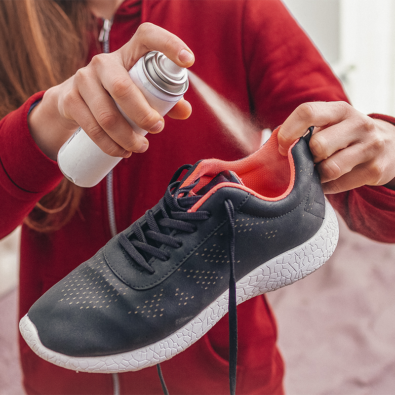 A young woman spraying deodorant on sweaty running shoes for eliminate unpleasant, bad smell. Shoe shine and care. Sport footwear needs in cleaning and odor removal.