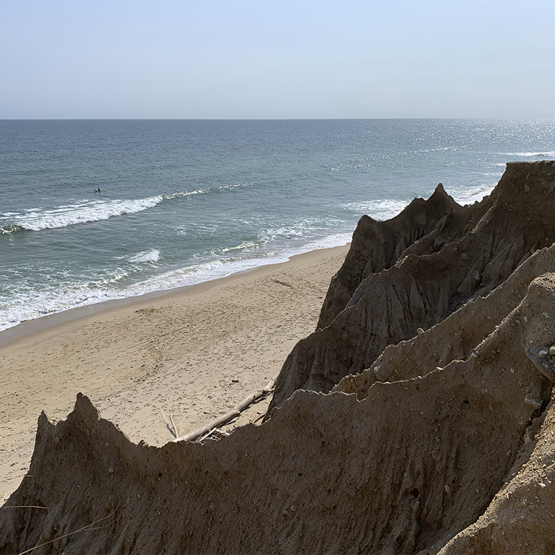 Cliffs edge overlooking the ocean and a lone surfer at Shadmoor State Park in Montauk, Long Island, New York